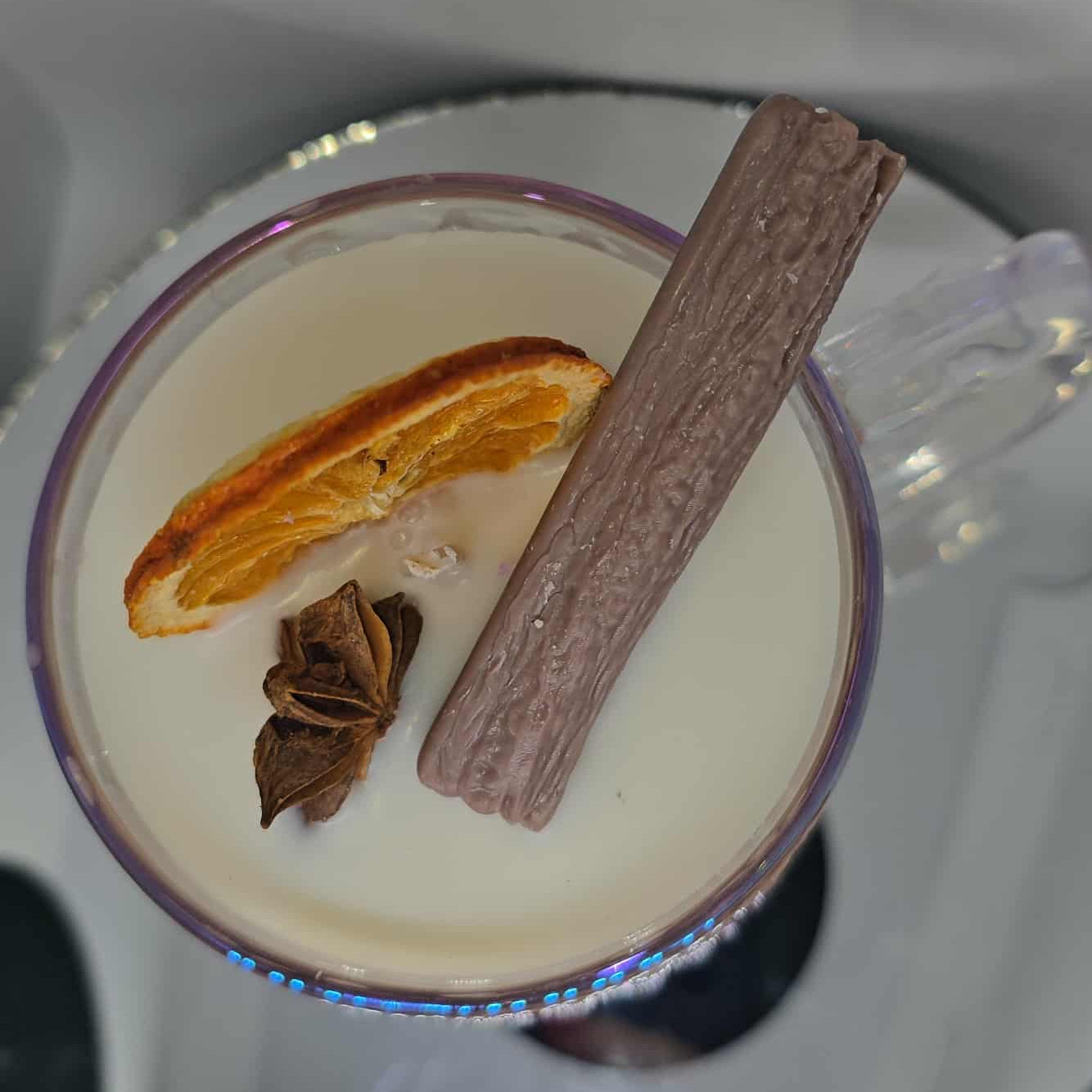 Close-up of a drink with an orange slice, cinnamon stick, and star anise on a white plate.