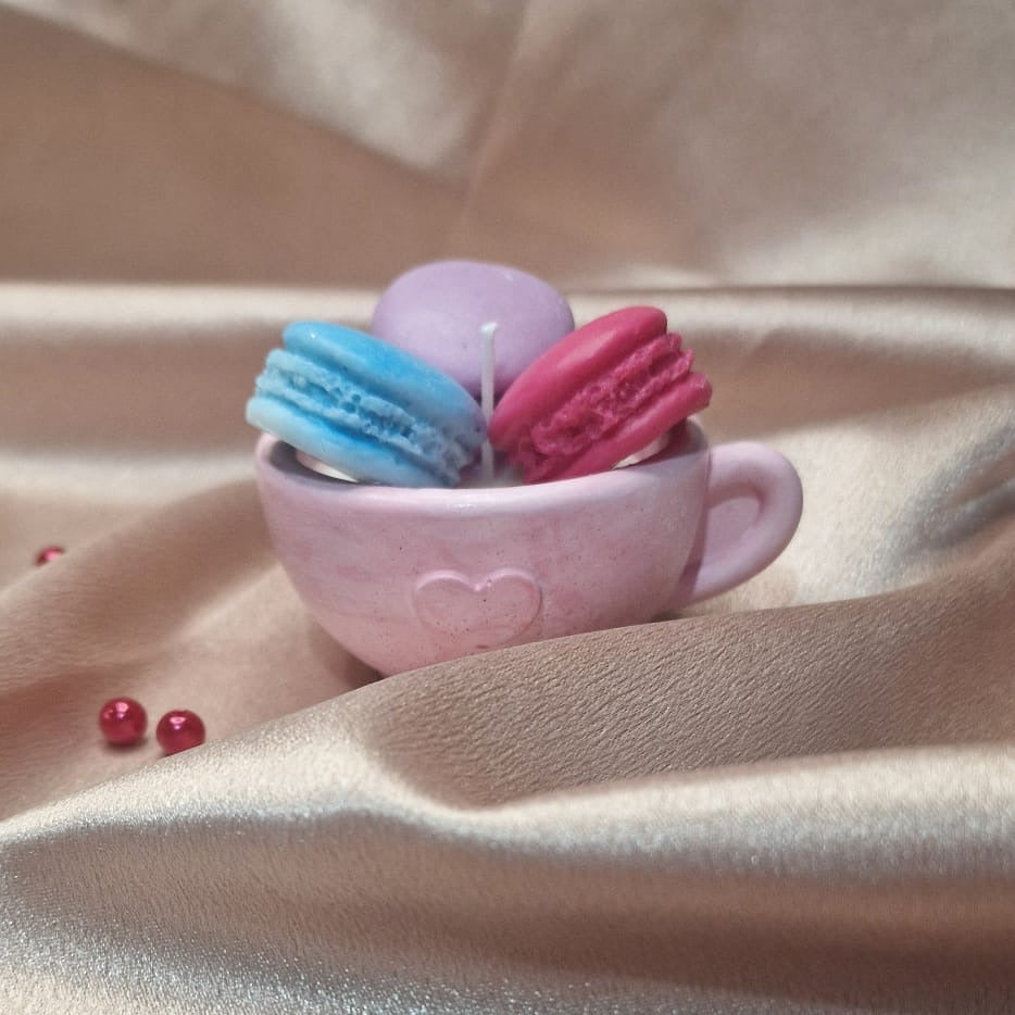 Small pink cup with colorful macarons on a beige fabric background