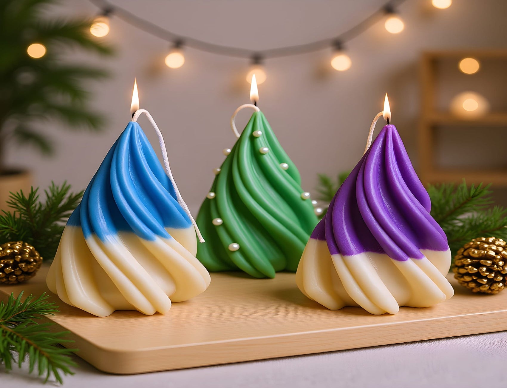 Three colorful Christmas tree-shaped candles on a wooden board with string lights in the background.
