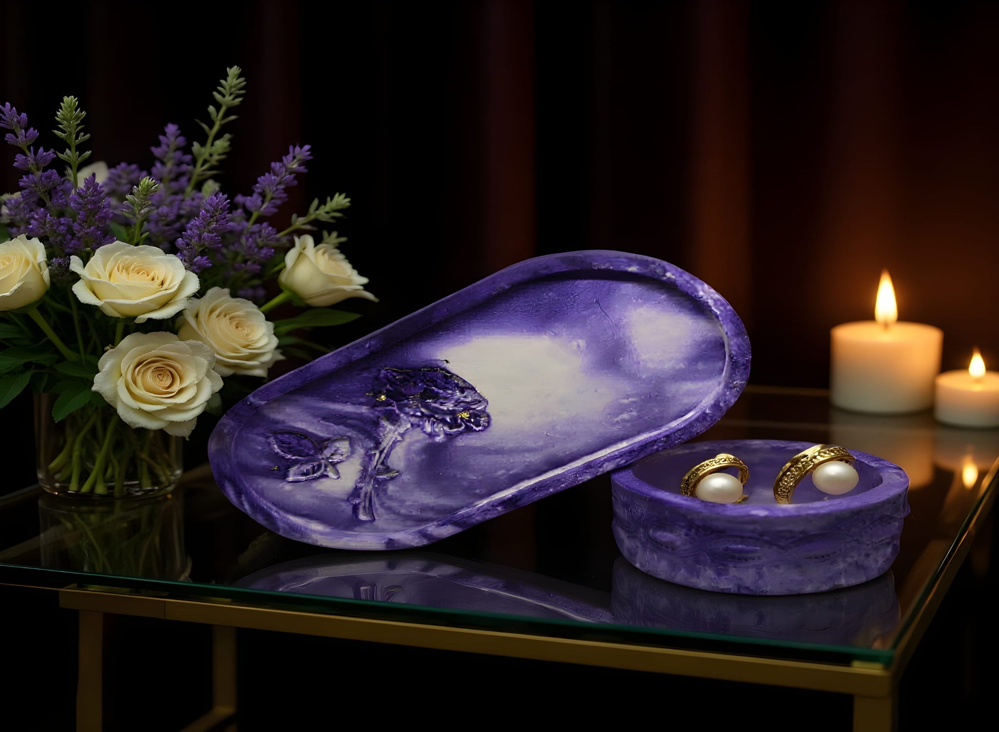 Purple jewelry box with floral design on a glass table with candles and flowers.