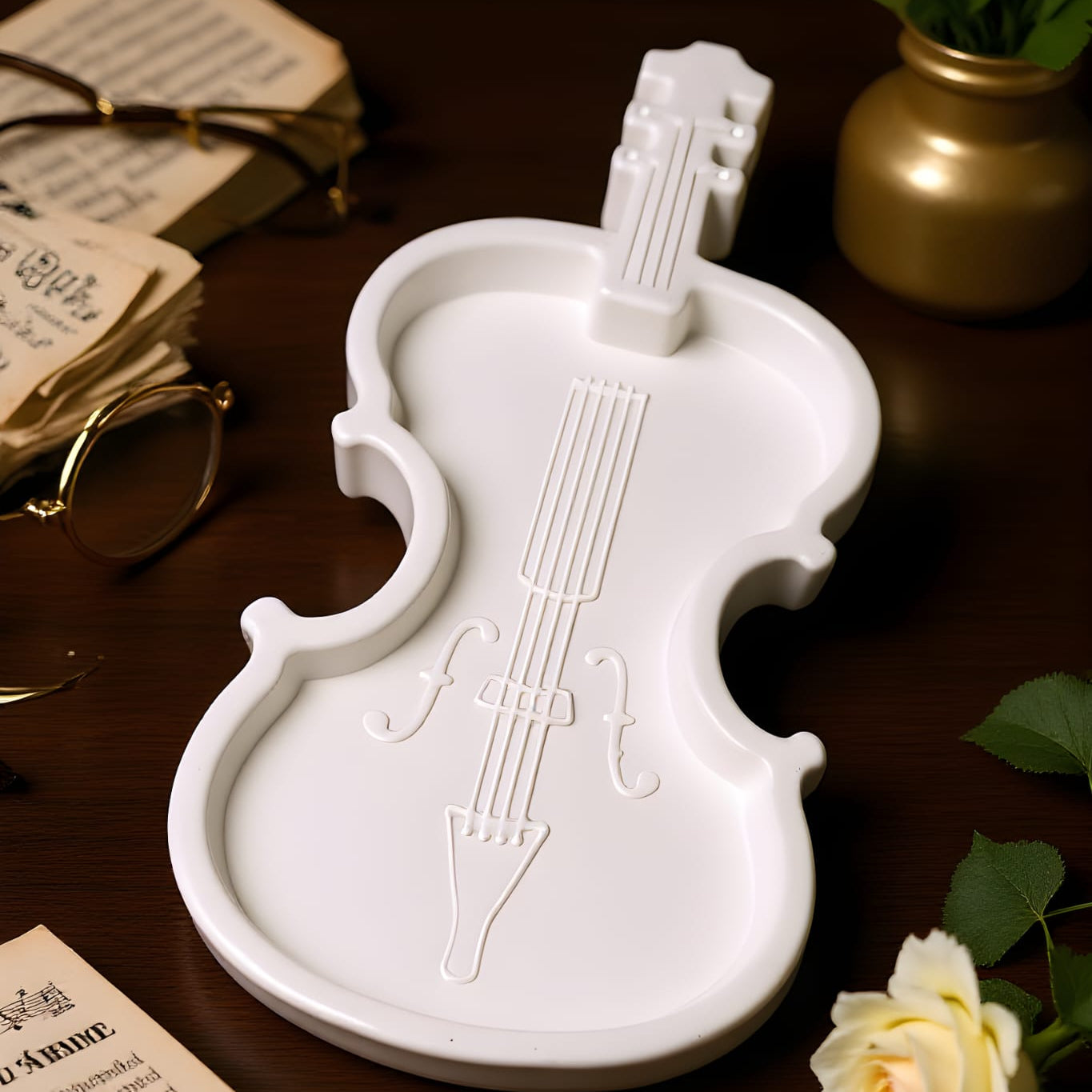 White violin-shaped dish on a wooden surface with books and a rose.